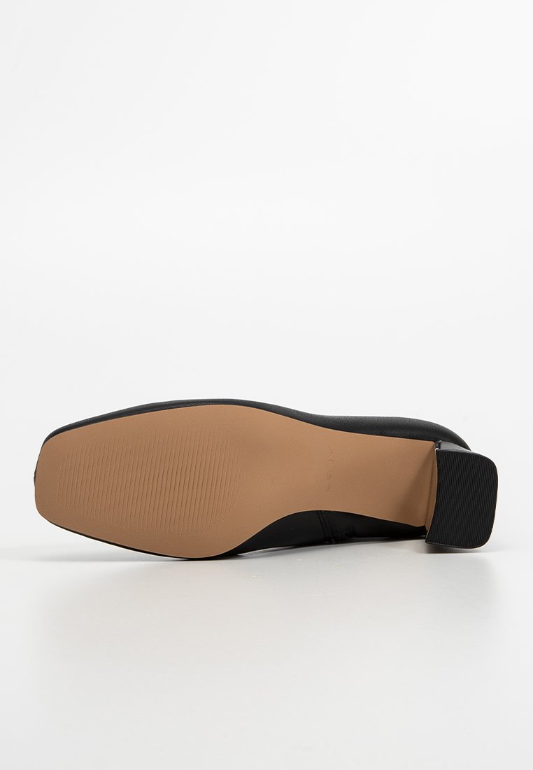 Suela de un zapato de cuero negro con fondo de goma marrón claro y tacón cuadrado negro, mostrada sobre un fondo blanco.