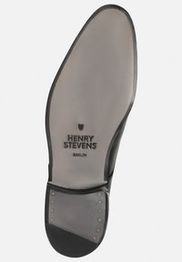 Semelle en cuir noir avec embout arrondi, marque en relief "HENRY STEVENS BERLIN", et clous métalliques le long du bord, texture lisse.