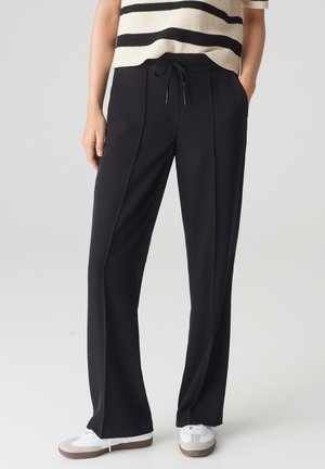 Black wide-leg pants with a drawstring waistband, featuring vertical seams for tailored fit. Worn with a striped top and white sneakers.