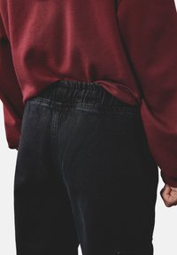 Burgundowa bluza zestawiona z wysokimi jeansami w kolorze czarnym, które mają elastyczny pas, gładką fakturę i delikatne detale przeszyć.