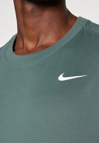 Zielona bawełniana koszulka z okrągłym dekoltem, z białym logo Nike po lewej stronie klatki piersiowej. Gładka faktura, krótkie rękawy.