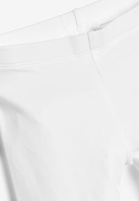 Leggings bianchi in cotone con una texture liscia, caratterizzati da un design semplice e una morbida vita. Il tessuto appare leggero ed elasticizzato.