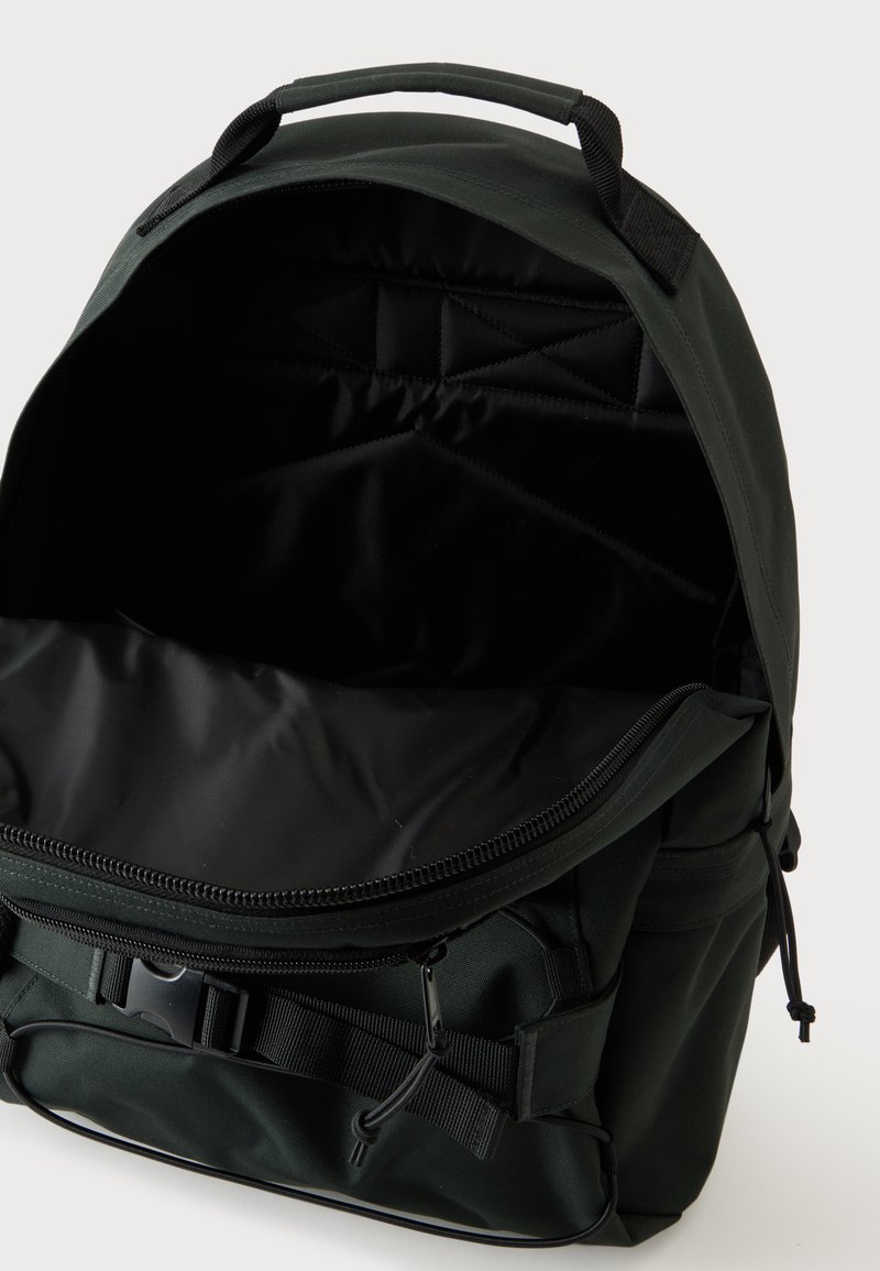 Schwarzer Rucksack mit offenem Hauptfach, gepolstertem Innenraum, oberem Griff, vorderem Schnallenriemen und seitlichen Taschen sichtbar vor einfachem Hintergrund.
