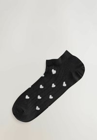 Zwarte enkelsok met wit hartjespatroon gelijkmatig verdeeld over de stof op een effen lichte achtergrond.