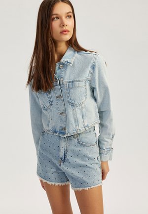 Chaqueta de mezclilla corta de color azul claro con cierre de botones y dos bolsillos en el pecho, acompañada de pantalones cortos a juego decorados con patrones de puntos negros.