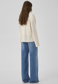 Pull beige tricoté avec un ourlet côtelé et des manches larges, associé à un jean à jambe large taille haute bleu clair. Texture lisse, design décontracté.