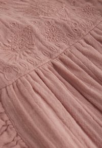 Staubrosa Textilie mit filigraner Stickerei in Blumenmustern und gerafften Falten, die eine weiche, strukturierte Oberfläche präsentiert.