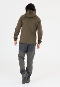 Bruine hoodie-jack en grijze broek gemaakt van textuurmaterialen, met contrasterende panelen en een aansluitend ontwerp, geschikt voor buitenactiviteiten.