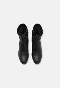 Bottes noires en cuir à la cheville avec une texture lisse, des bouts pointus et deux fermetures éclair sur les côtés, présentant un design simple et épuré.