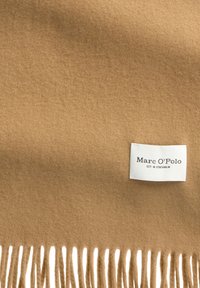 Brązowy wełniany szal z frędzlami, z białą metką z napisem "Marc O'Polo EST. W Sztokholmie." Miękka tekstura, prostokątny kształt.