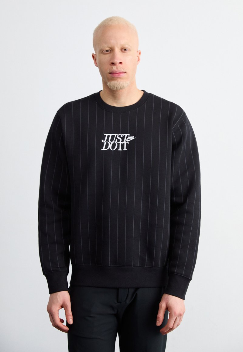 Fekete pulcsi fehér függőleges csíkokkal és egy "JUST DO IT" logóval. Kerek nyakkal és bordázott mandzsettákkal rendelkezik a testhez álló megjelenés érdekében.