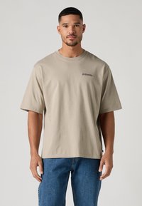 Smėlio spalvos medvilniniai marškinėliai trumpomis rankovėmis ir apvalia apykakle. Kairėje krūtinės pusėje yra nedidelis juodas logotipas. Lengvas audinys.