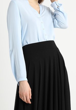 Blusa azzurra chiara a maniche lunghe con scollo a V e chiusure a bottone, abbinata a una gonna nera plissettata. Texture del tessuto liscia.