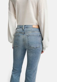 Jasnoniebieskie dżinsy z dopasowaną talią, z dwoma tylnymi kieszeniami i skórzaną metką na pasku. Noszone z kremowym, długim rękawem.