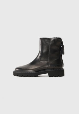 Botas de tobillo de cuero negro con punta redondeada, paneles elásticos laterales, una cremallera trasera y una suela de goma gruesa. Incluye un borlón decorativo.