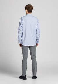 Ljusblå knapp-up skjorta, långärmad, med ryggsömmar, i kombination med grå stickade byxor och svarta skor. Enkel, avslappnad design.