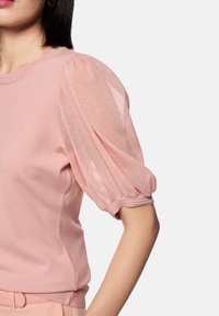 Light pink top featuring short puff sleeves made of sheer material, with a rounded neckline and subtle side seam detailing.