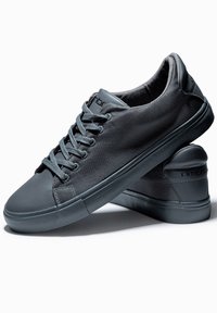 Grå sneakers med en strukturerad mesh-övre och en slät gummisula. Funktioner inkluderar snören, en rundad tå och en logotyp på hälen.