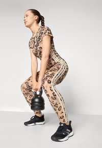 Sett med leopardmønster aktivtøy med korte ermer og sidelister, kombinert med svarte joggesko; holder en svart kettlebell.