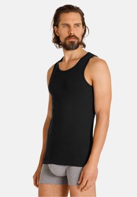 Canottiera nera in cotone, con scollatura rotonda e spalline larghe. Indossata con boxer grigi, che evidenziano una silhouette aderente.