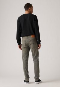 Faded grey jeans with a straight cut, paired with a black long-sleeve shirt. Features a leather waistband label and casual black shoes.