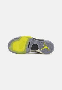 Semelle d'une basket avec une bande de roulement grise et jaune néon, présentant un logo Jumpman noir et jaune néon près de la zone des orteils.