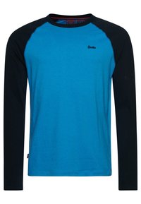 Sininen pitkähihainen t-paita mustilla raglan-hihalla. Valmistettu puuvillasta, jossa on pyöreä kaula-aukko ja pieni logo rinnassa.