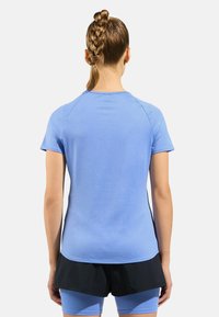 Light blue athletic shirt with short sleeves, featuring a rounded neckline and smooth texture. Paired with black shorts.