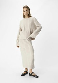 Maglione lavorato a maglia beige chiaro con texture a coste, abbinato a una gonna midi coordinata. Accessori: ballerine nere con dettagli a fibbia.