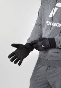 Schwarze Handschuhe mit strukturiertem Griff, taillierter Passform und Daumenöffnung. Kombiniert mit einem grauen Hoodie, der eine sportliche Ästhetik zeigt.