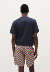 T-shirt en coton marine à manches courtes associé à un short à motif chevrons orange et bleu, doté d'une ceinture élastique et de poches.