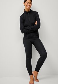 Zwarte sportieve zip-up top met lange mouwen en aansluitende zwarte leggings. Glad materiaal, strakke pasvorm en platte naden. Geen zichtbare patronen of logo's.