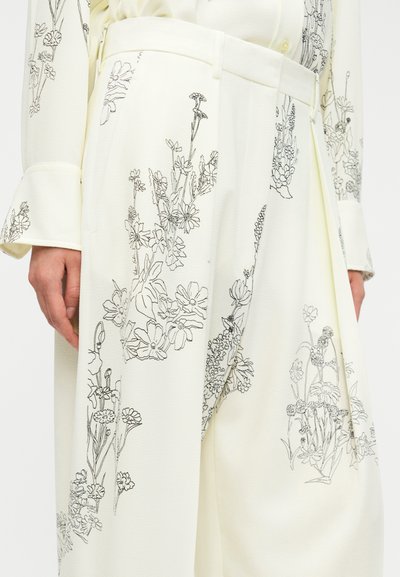 Παντελόνια με φαρδιά μπατζάκια και λουλουδένιο σχέδιο σε ανοιχτό κίτρινο ύφασμα με μαύρες γραμμικές απεικονίσεις λουλουδιών. Διαθέτουν εφαρμοστό ζωνάκι στη μέση και πλαϊνές τσέπες.