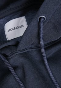 Sudadera azul marino con una textura de tela suave, cordones ajustables y una etiqueta tejida con "JACK & JONES" visible en el interior del cuello.