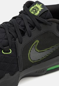 Baskets noires avec lacets noirs, panneaux texturés, accents vert néon, un swoosh blanc Nike et un logo tête de lion vert néon sur la languette.