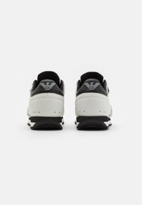 Svarta och vita sneakers i texturerat läder, med låg profil, vadderad krage och randig sula. Logotyp bakpå.