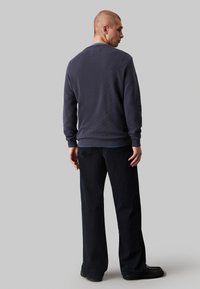Camicia a maniche lunghe blu navy con un motivo testurizzato, dotata di collo a giro e vestibilità rilassata, abbinata a pantaloni larghi scuri e calzature nere.