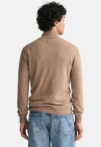 Brauner Strickpullover mit hohem Kragen, gerippten Bündchen und Saum, kombiniert mit hellblauen Jeans. Weiche Textur sichtbar.