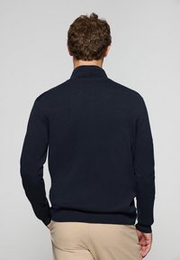 Suéter azul marino con cuello alto, textura de punto y puños acanalados. Presenta un diseño limpio, sin patrones ni herrajes visibles.