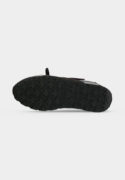 Semelle de chaussure noire avec des motifs de traction profonds en forme de feuille d’érable et une petite étiquette de marque rectangulaire au centre.