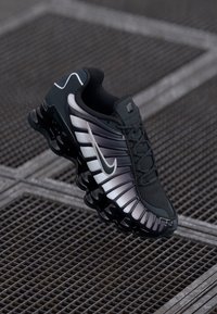 Sapatilha atlética preta e cinza com um upper texturizado, design exclusivo em forma de onda e gola acolchoada, apresentando um logótipo swoosh proeminente e sola acolchoada.