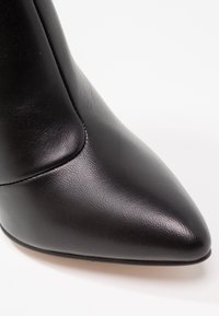 Bottine noire à bout pointu, fabriquée en cuir lisse. Design épuré avec des coutures discrètes et un talon fin.