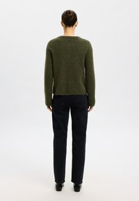 Grønn, teksturert genser med rund hals og lange ermer, kombinert med svarte jeans med rette ben. Bakfra vises et litt kortere design.