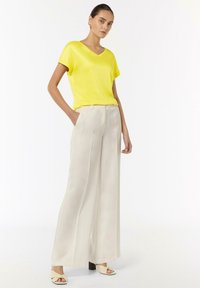 Żółta koszulka z dekoltem w serek w połączeniu z kremowymi spodniami o szerokich nogawkach. Ubranie charakteryzuje się gładką fakturą i luźnym krojem, z kieszeniami bocznymi w spodniach.