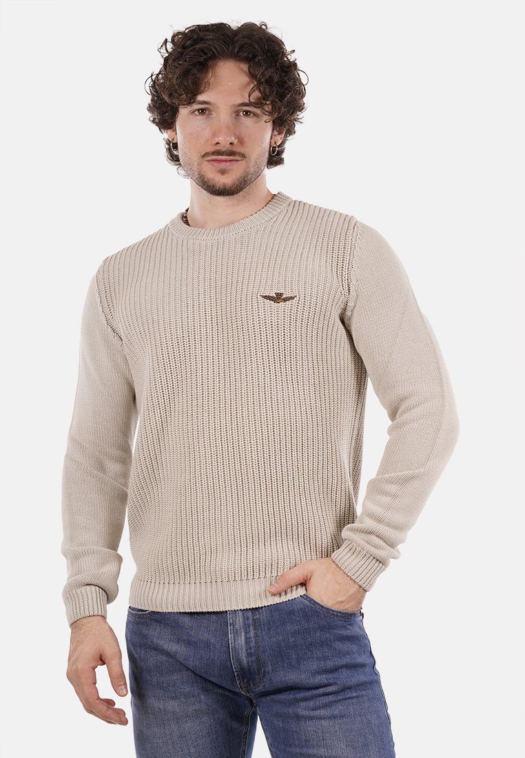 Maglione beige lavorato a maglia con collo rotondo e maniche lunghe. Presenta una trama a costine e un piccolo logo ricamato sul lato sinistro del petto.