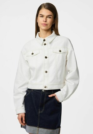 Avskuren vit denimjacka med knäppning framtill, två bröstfickor och långa ärmar, med kontrasterande sömmar och bronsknappar.