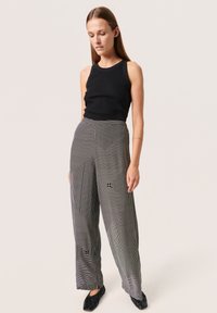 Top a manica lunga nero a coste abbinato a pantaloni a gamba larga con un motivo a righe geometriche in bianco e nero, tessuto liscio e vestibilità rilassata.