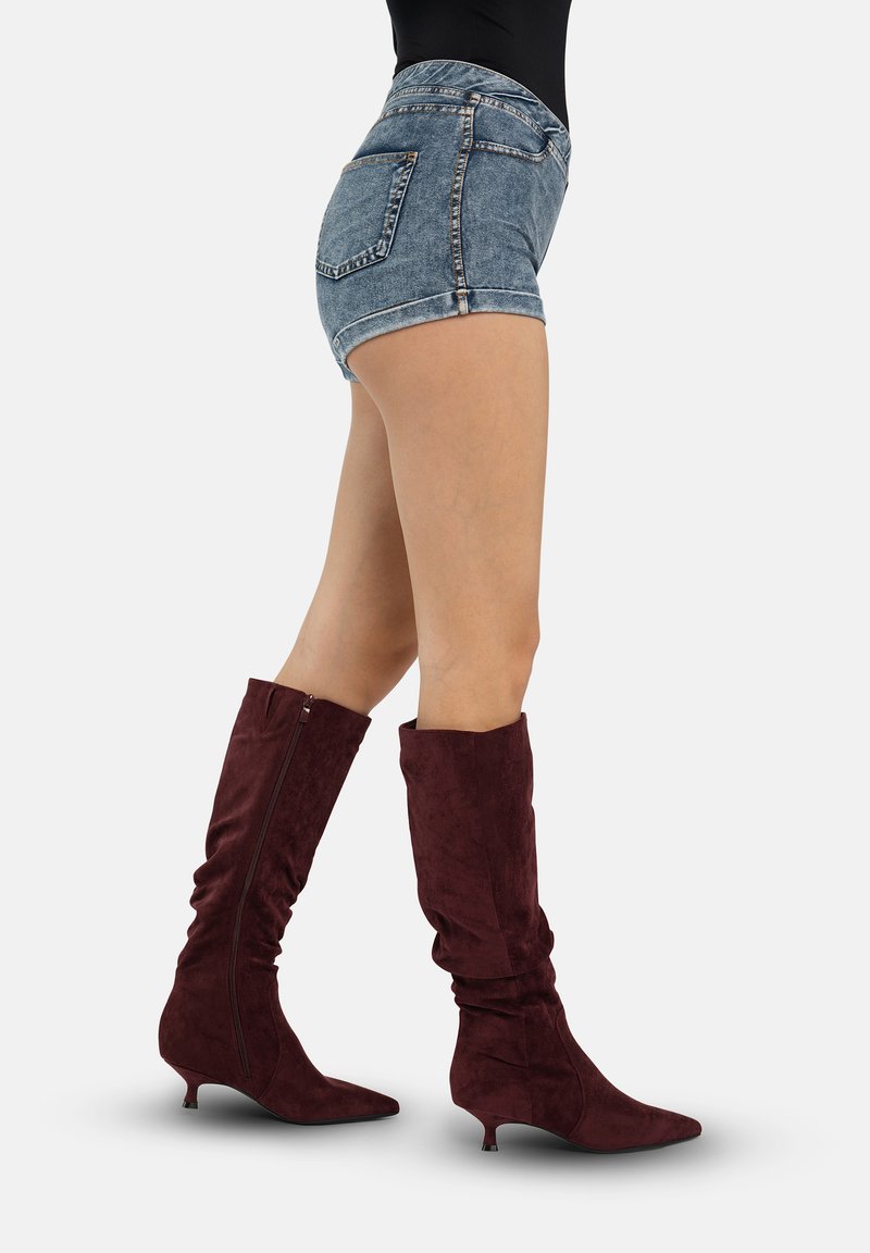 Bottes hautes en daim bordeaux à effet décontracté, bout pointu et petit talon kitten. Portées avec un short en jean taille haute.