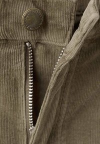 Tessuto di velluto a coste verde oliva con costine verticali, caratterizzato da una cerniera metallica argento e dettagli con bottoni rotondi in bronzo.