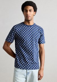 Μπλε βαμβακερό T-shirt σε σκούρο ναυτικό χρώμα με λευκά κυκλικά και ανθισμένα σχέδια, κοντά μανίκια και στρογγυλή λαιμόκοψη. Κλασική εφαρμογή με λεία υφή.